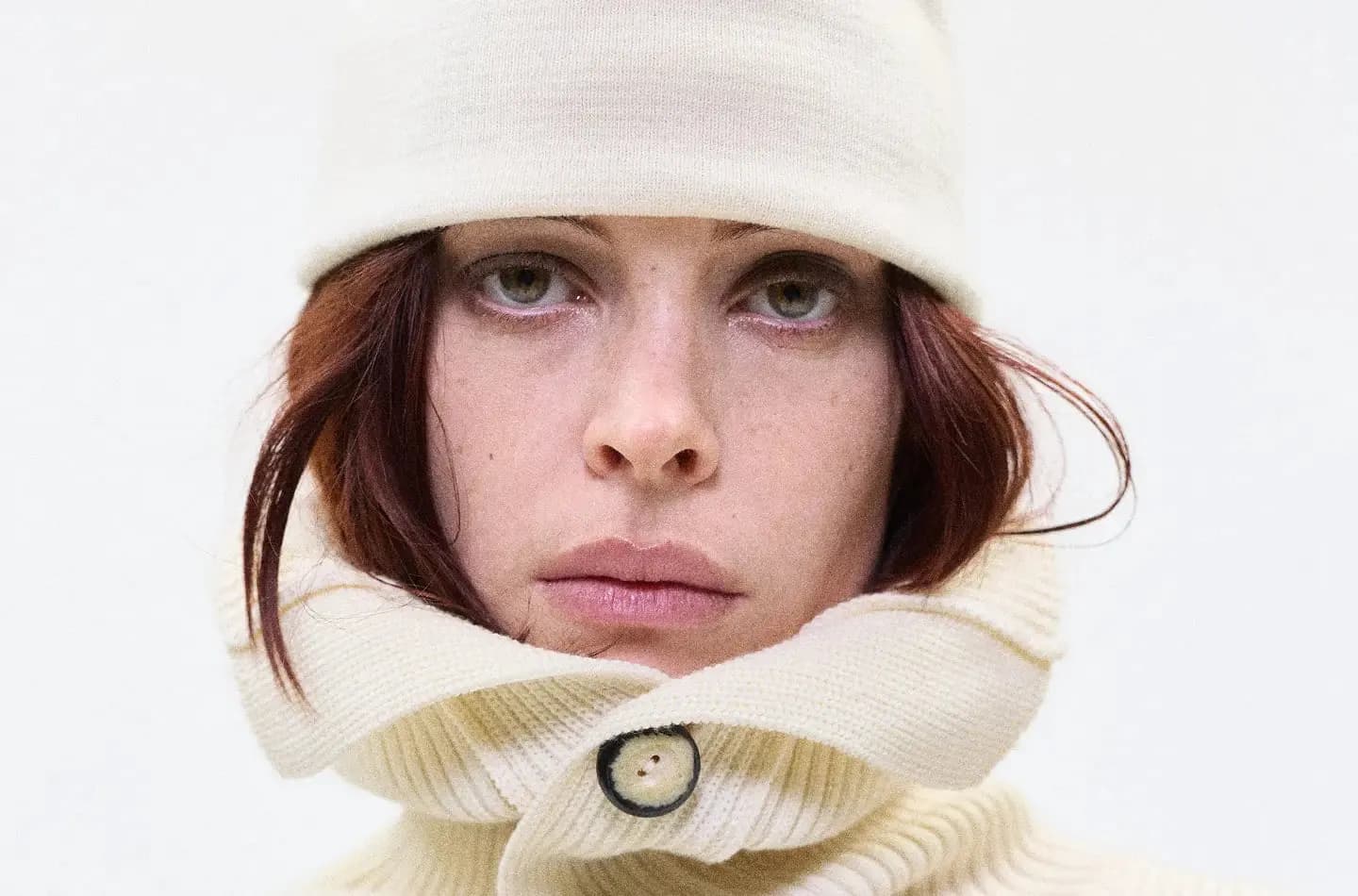 A model in a cream Monphell knit hat and high buttoned collar